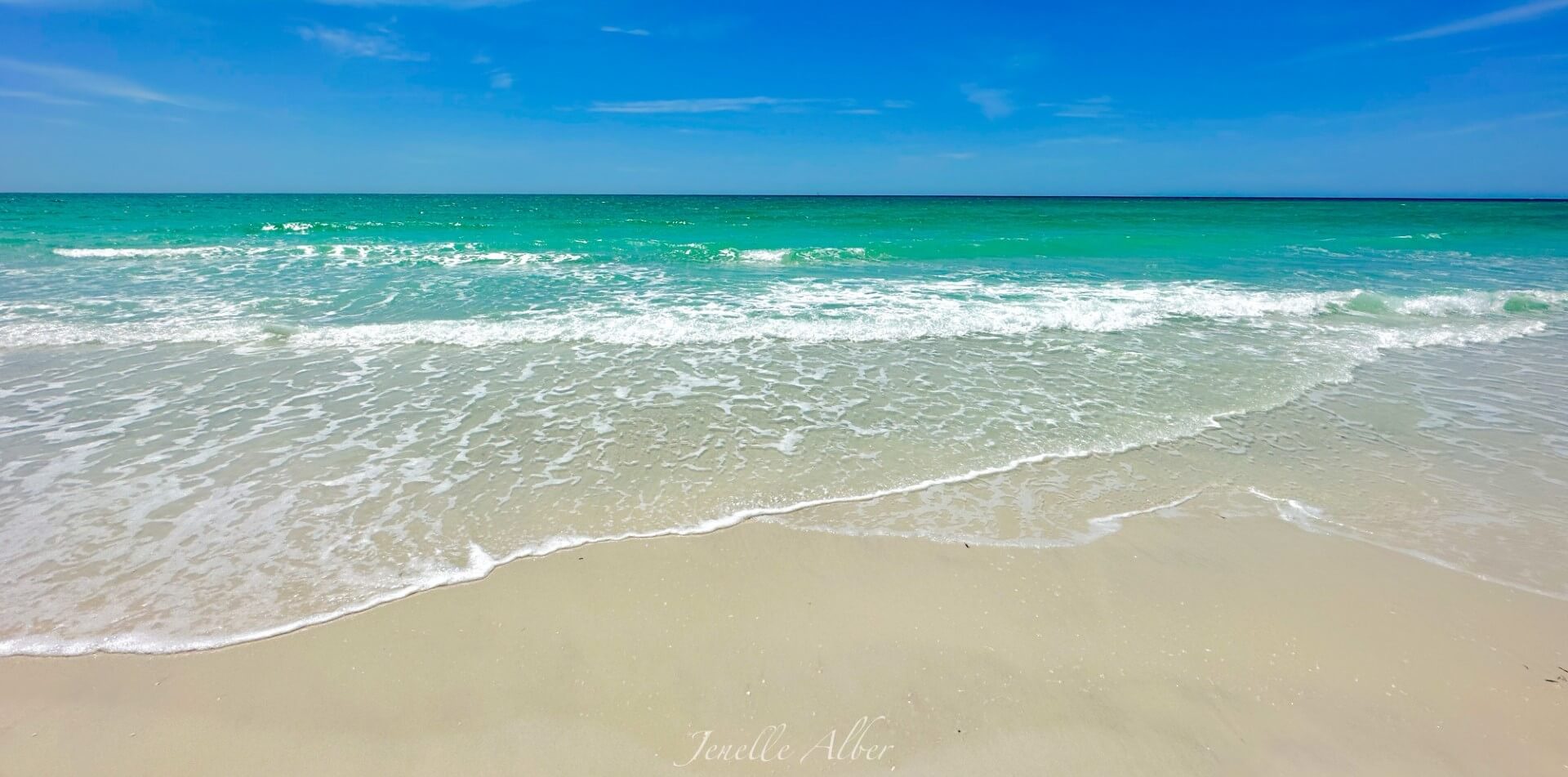 Photo of the beach with the bright blue ocean water rolling over the sand.