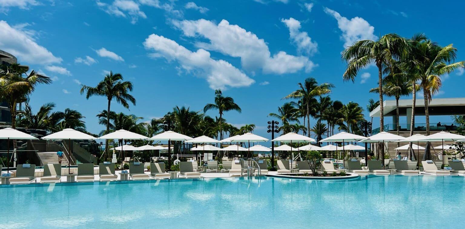 Picture of a hotel pool with white umbrellas and chairs lined up along the side of the pool.