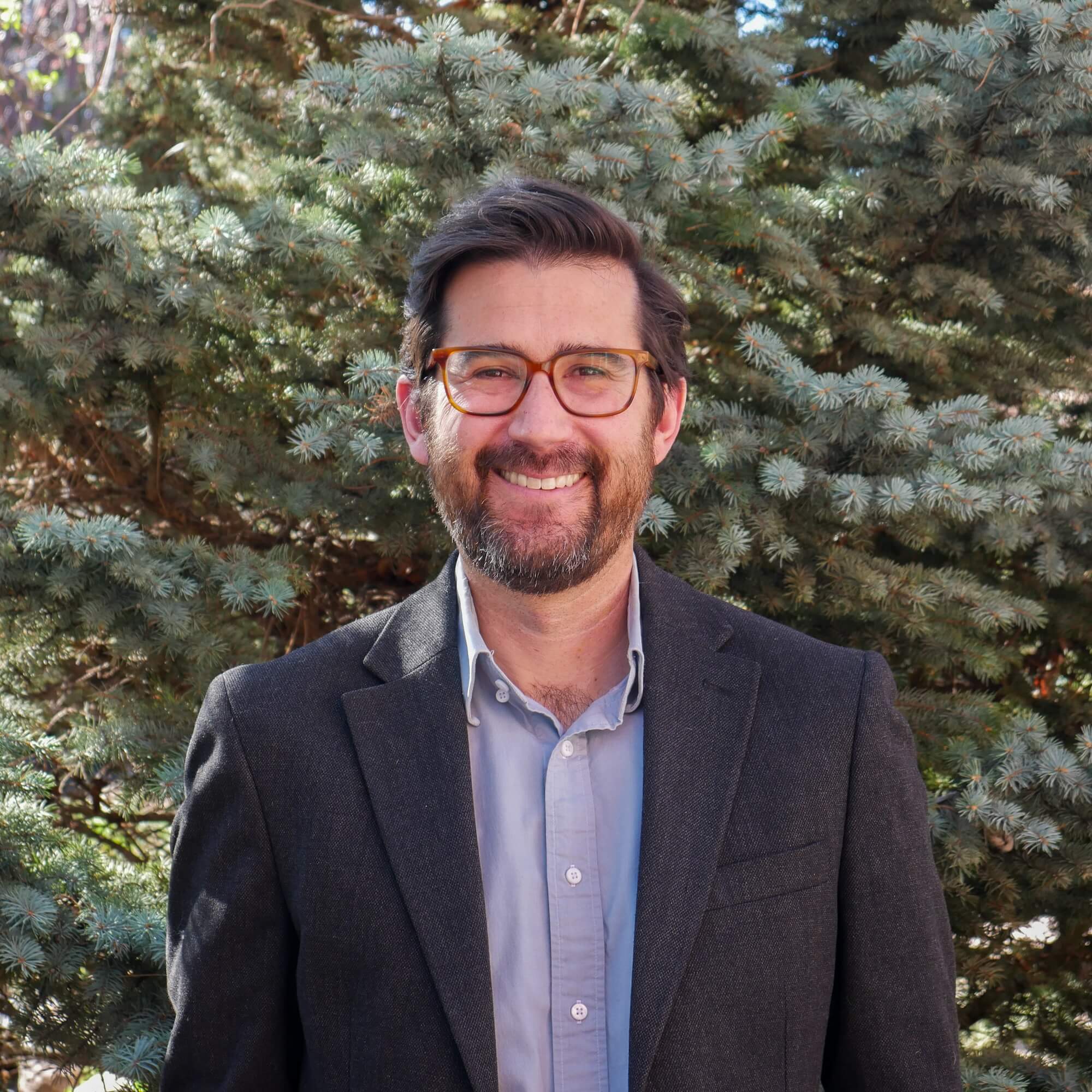 Aaron Citron Headshot in front of a large evergreen