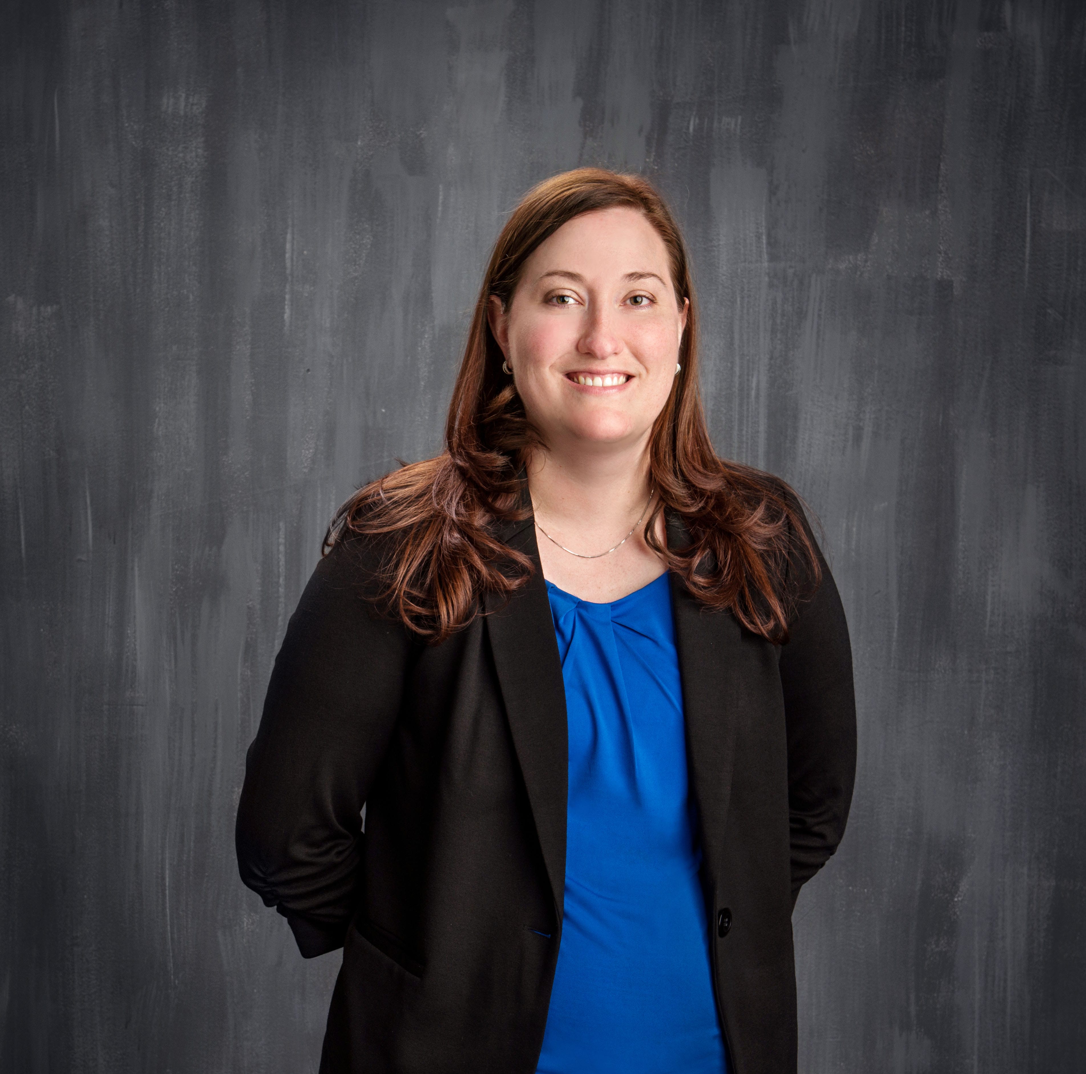 Picture of board member Stephanie Enders. She is smiling and wearing a blue shirt with black blazer, her hair is past her shoulders and an auburn brown.