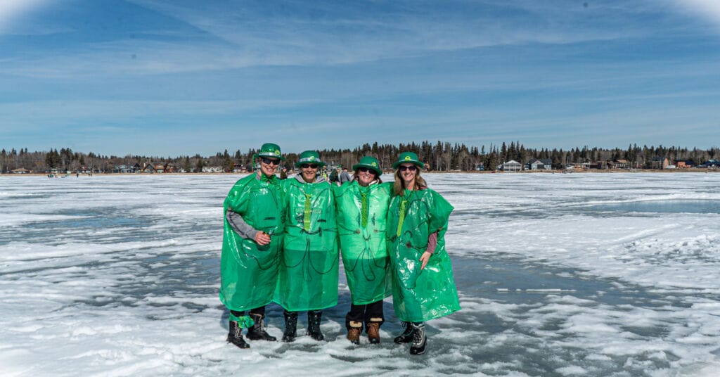 A group of people stand on a frozen lake in green plastic costumes and hats