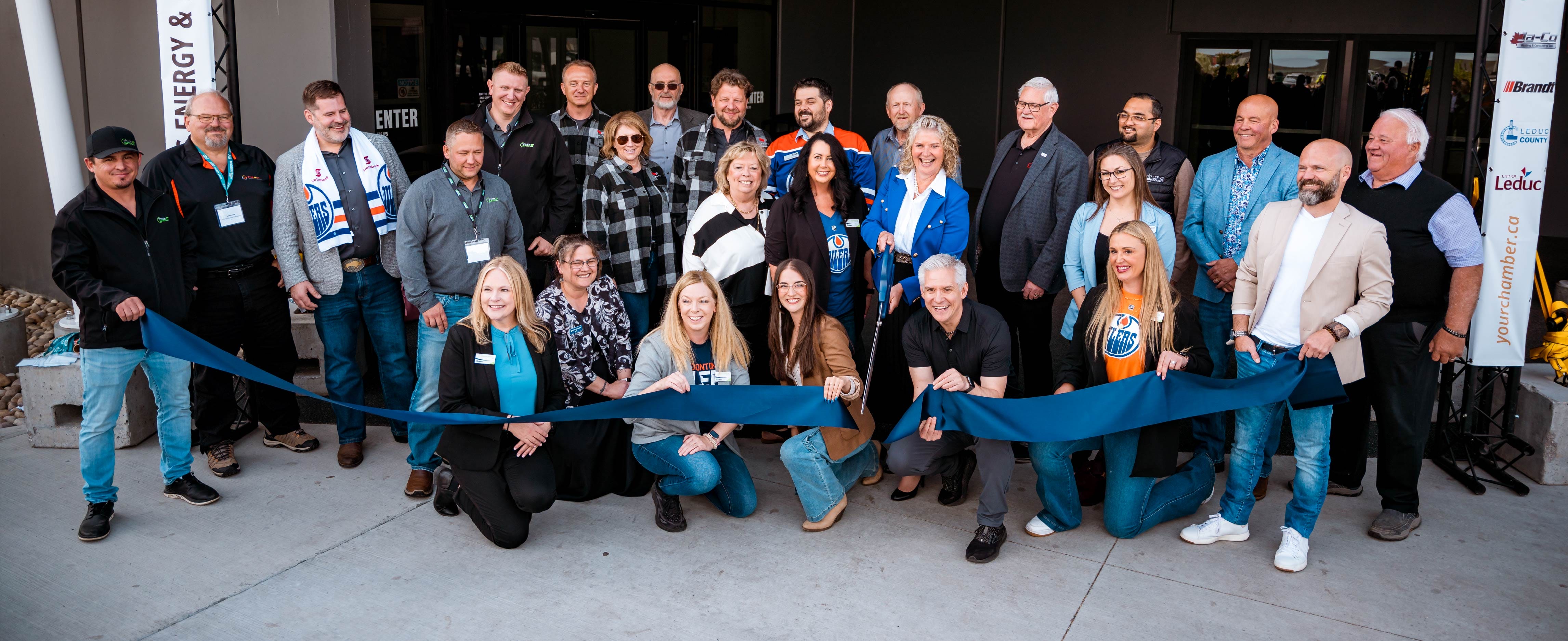 A large group of smiling people are lined up for a ribbon cutting.