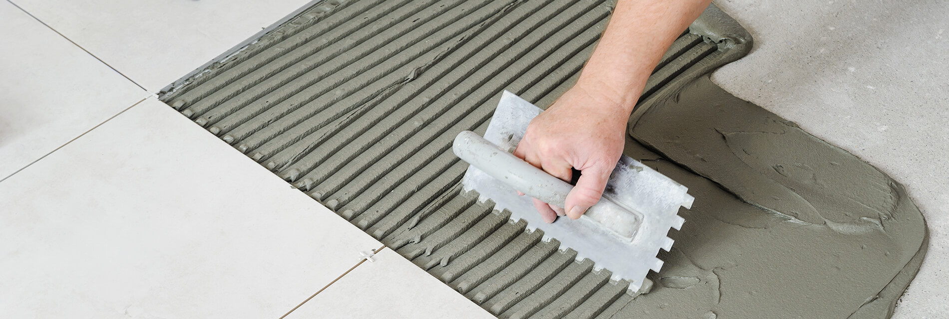 The worker's hand is putting tiles adhesive to the wall