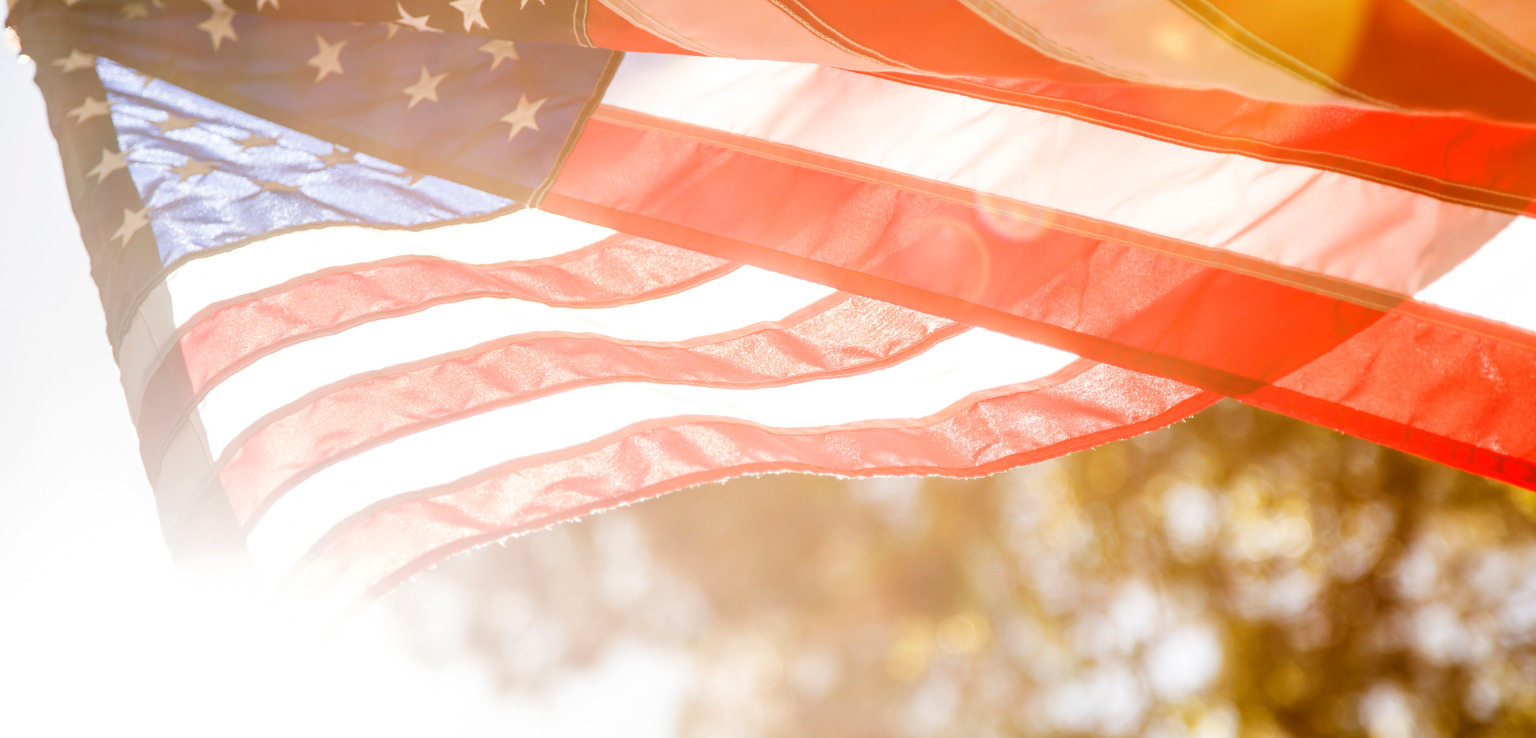 1. An American flag waves gently in the sunlight against a clear blue sky.