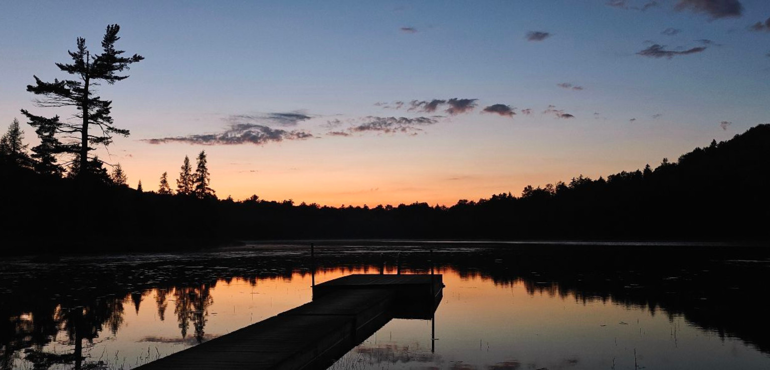 A serene dock extends over a lake, bathed in warm hues of sunset, reflecting on the water's surface.