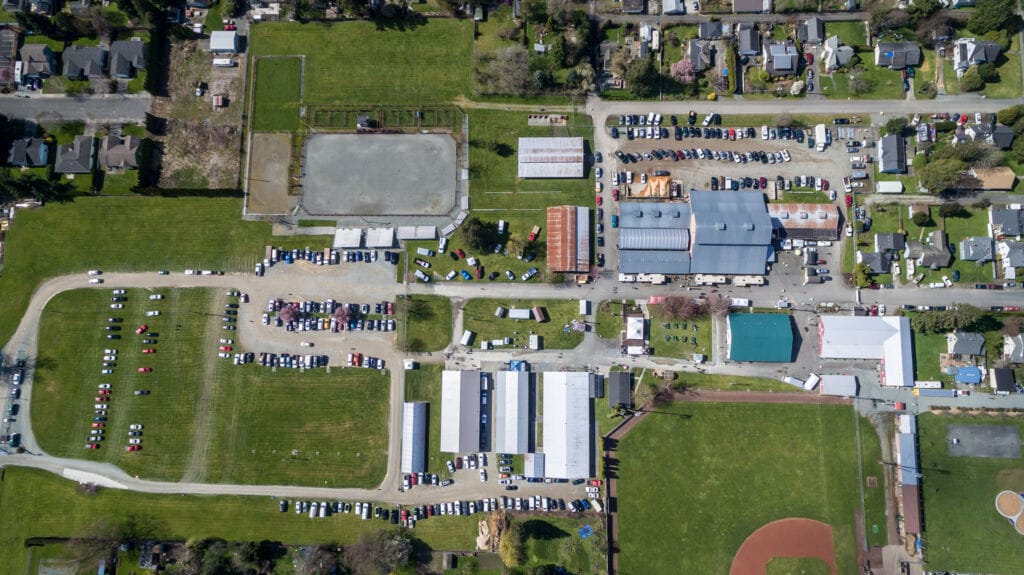 Aerial view of the Skagit County Fairgrounds in Mount Vernon, Washington, showing large event barns, grassy fields, parking areas, and nearby residential neighborhoods