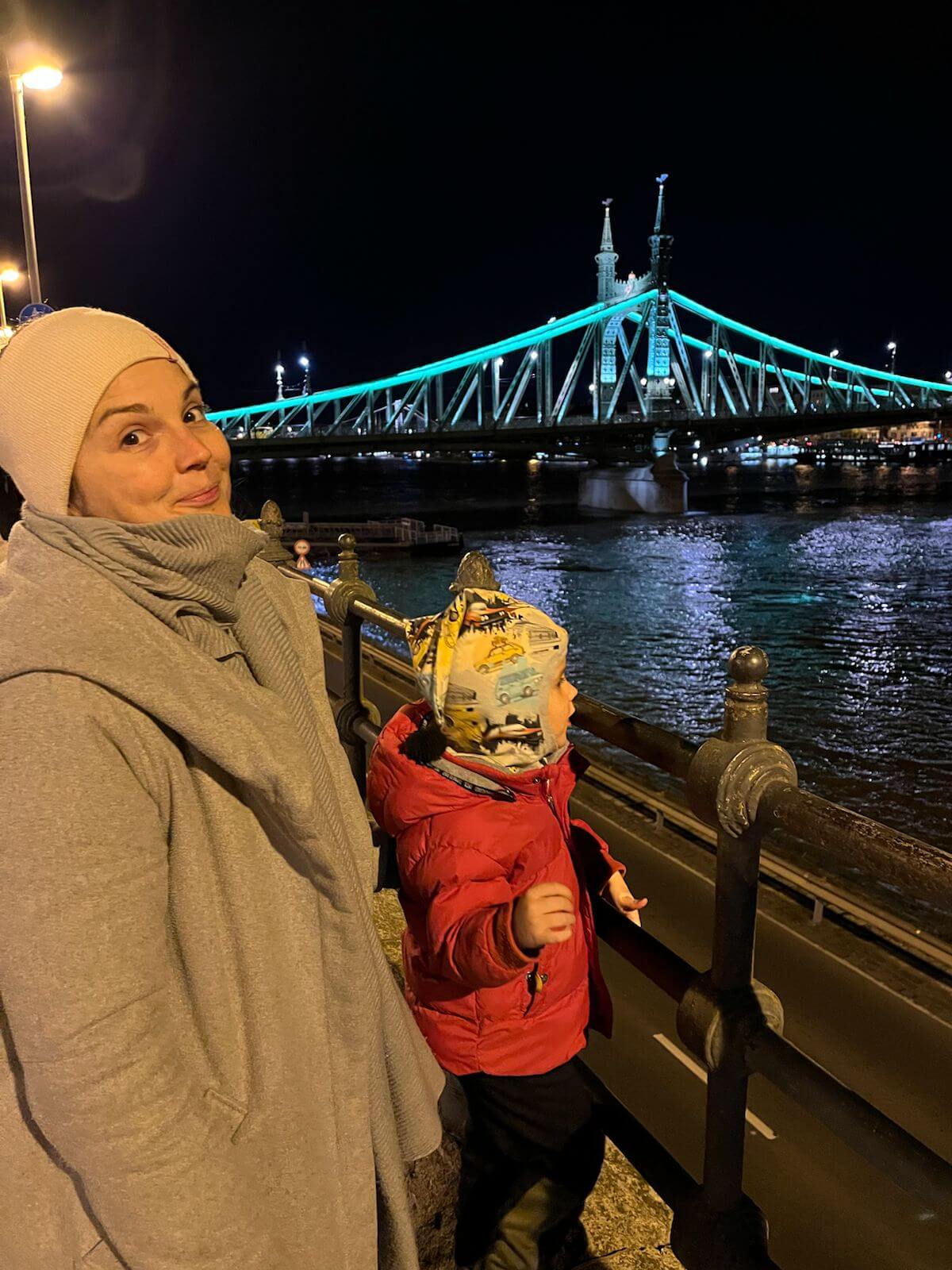 Woman and child in front of lit-up bridge