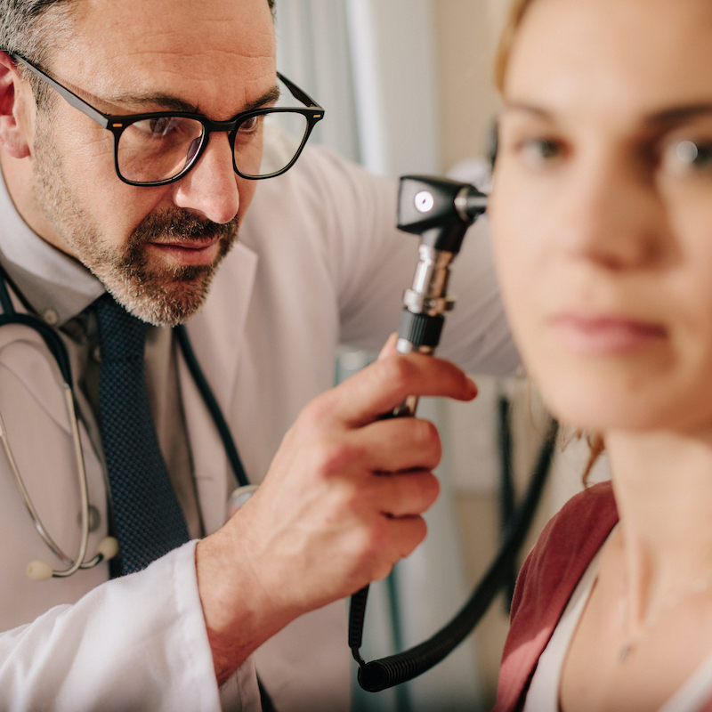 ENT doctor checking ear with otoscope of woman patient at hospital. Physician examining ear of female patient with an instrument. (ENT doctor checking ear with otoscope of woman patient at hospital. Physician examining ear of female patient with an in
