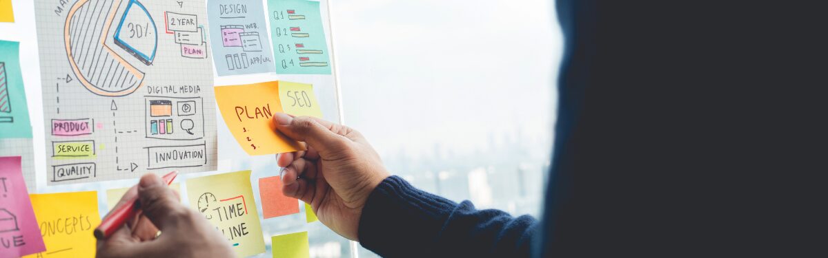 Person placing sticky notes on a glass wall during a collaborative planning session.