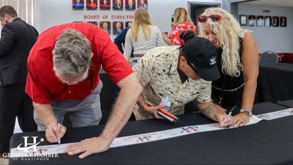 People signing Greater Chamber of Harlingen ribbon for ribbon-cutting event
