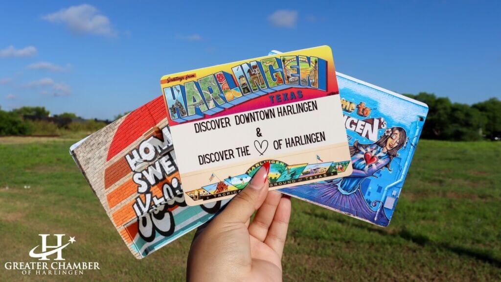 Hand holding colorful postcards promoting Discover Downtown Harlingen and Where To Shop Local In Harlingen Texas, highlighting the city’s vibrant local culture.