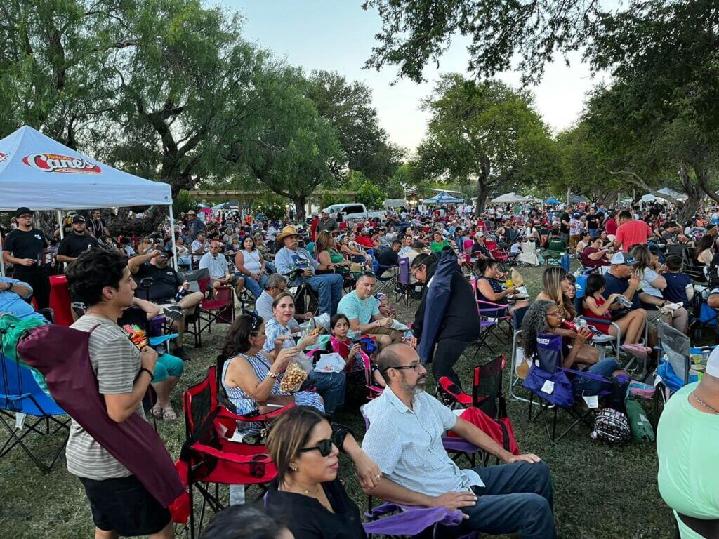 A large crowd gathers outdoors during a Harlingen event, with families, friends, and attendees seated across the lawn enjoying the program, reflecting the city’s strong community turnout and lively local gatherings.
