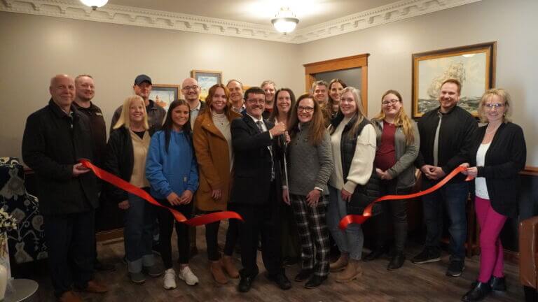 A photograph of the ribbon cutting for Carnall Law Office. Pictured in the photo holding the scissors is Andy Carnall, alongside members of the Wells County Chamber of Commerce.