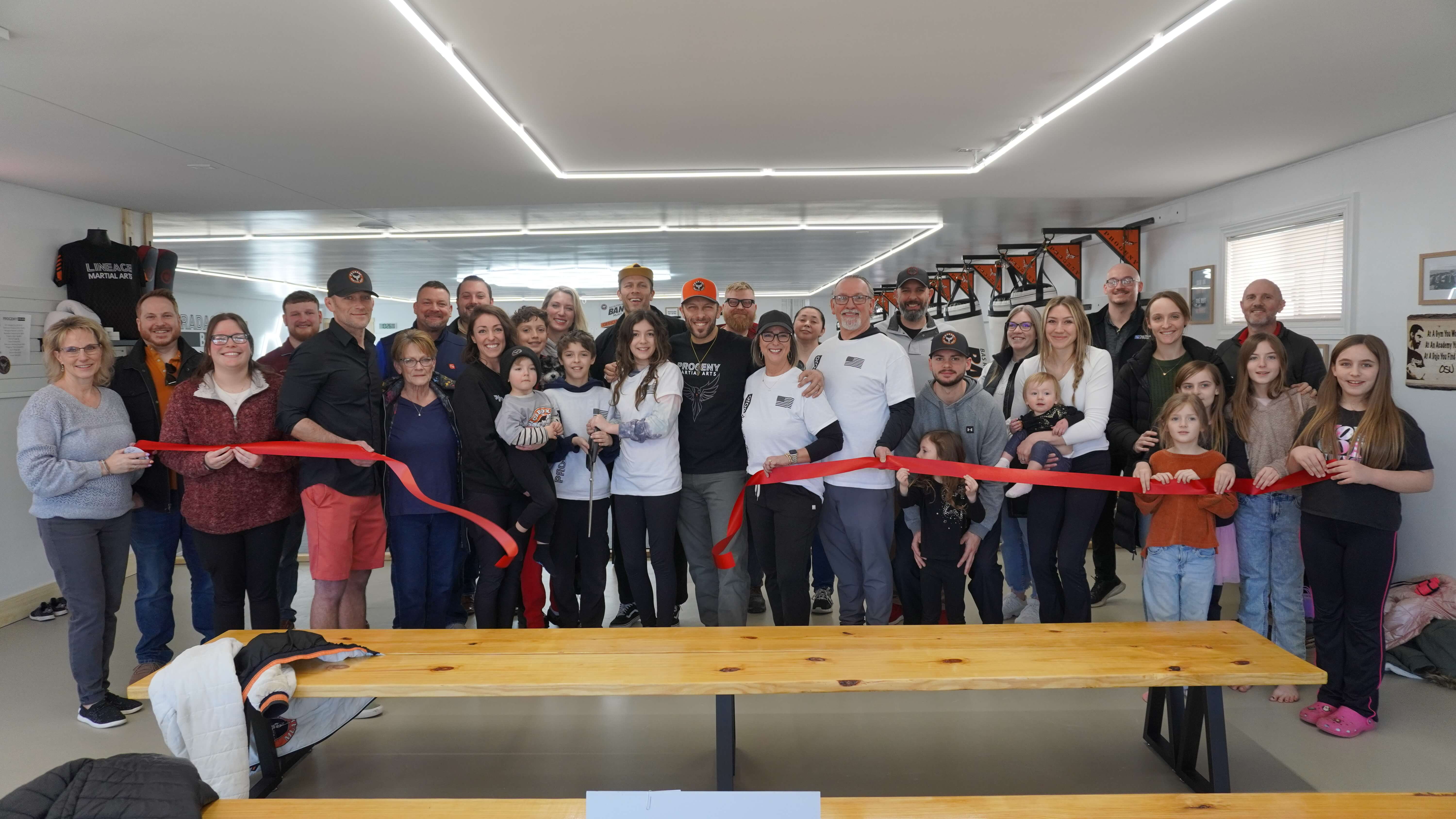 A large group of people cutting a ribbon consisting of the business owners, family, and friends of Progeny Dojo; in addition to members of the Wells County Chamber of Commerce and Chamber Ambassadors.