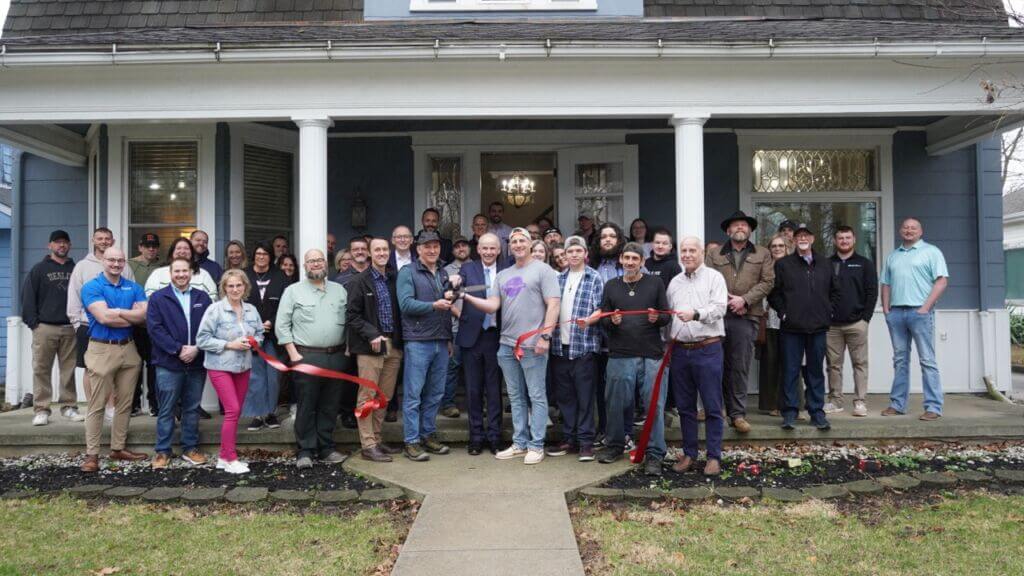 A photo of a large group of people standing in front of The Resilient House cutting a ribbon. The group includes Andy Yergler (the owner) with friends and family, members of the Chamber, Chamber Ambassadors, and other community members.