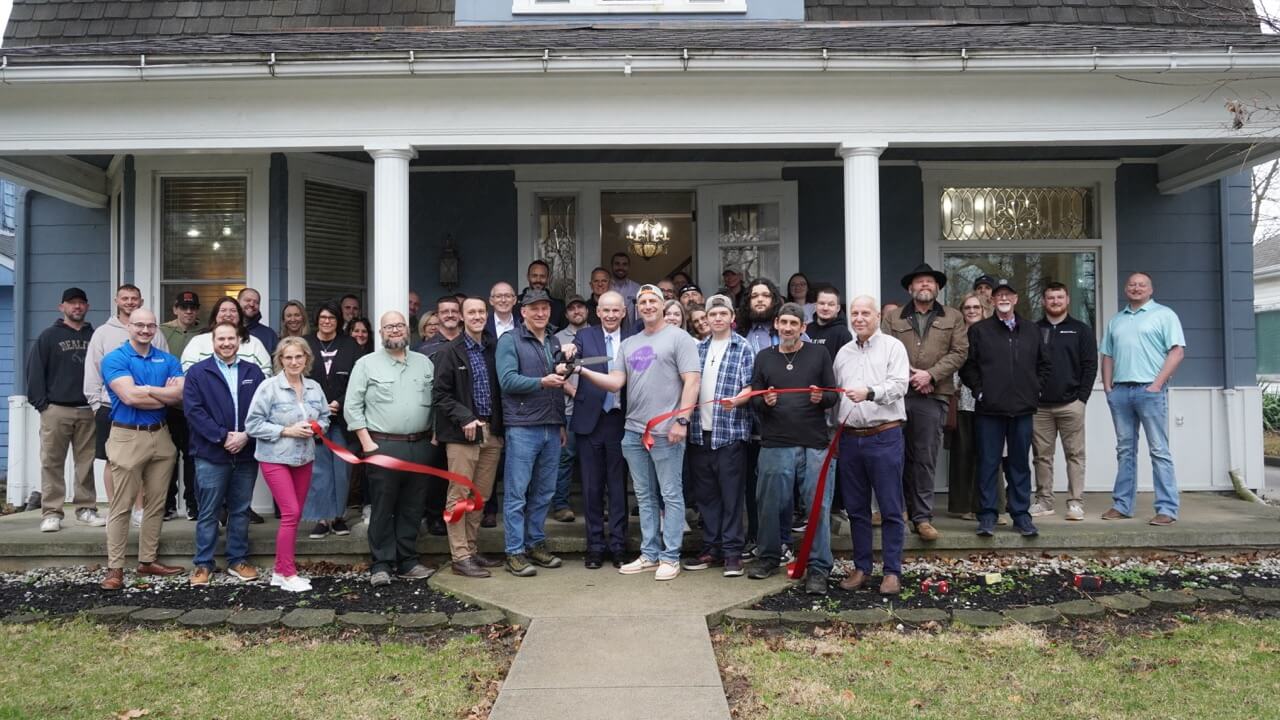 A photo of a large group of people standing in front of The Resilient House cutting a ribbon. The group includes Andy Yergler (the owner) with friends and family, members of the Chamber, Chamber Ambassadors, and other community members.