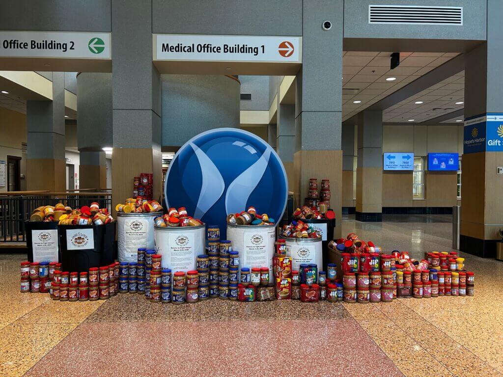 A photo showcasing hundreds of jars of peanut butter in front of the Lutheran Health Network logo in the lobby of a hospital.