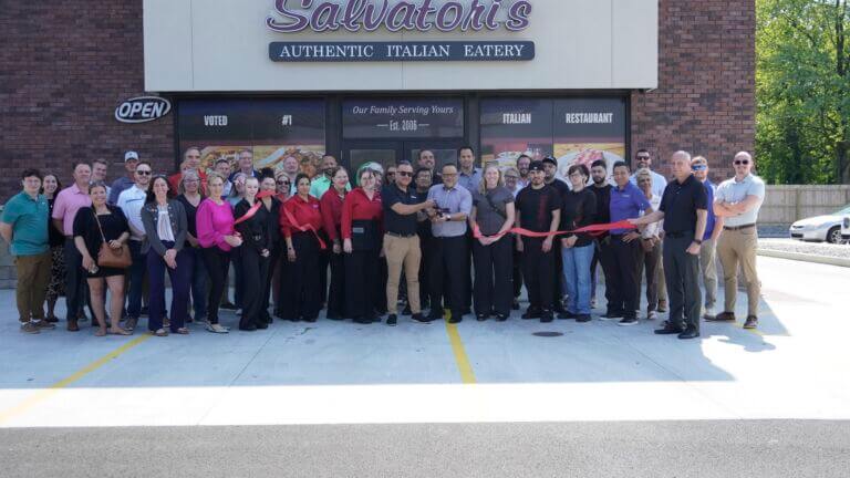 A ribbon cutting ceremony outside of the new Salvatori's location in Bluffton, Indiana. Pictured are members of staff from Salvatori's Chamber staff, Chamber ambassadors, and community members.