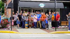 A photo of the ribbon cutting ceremony outside the entrance of Jamie's Cafe in Bluffton, IN. The group cutting the ribbon consists of Jamie's Cafe staff/employees, Chamber staff, Chamber ambassadors, and local community members.