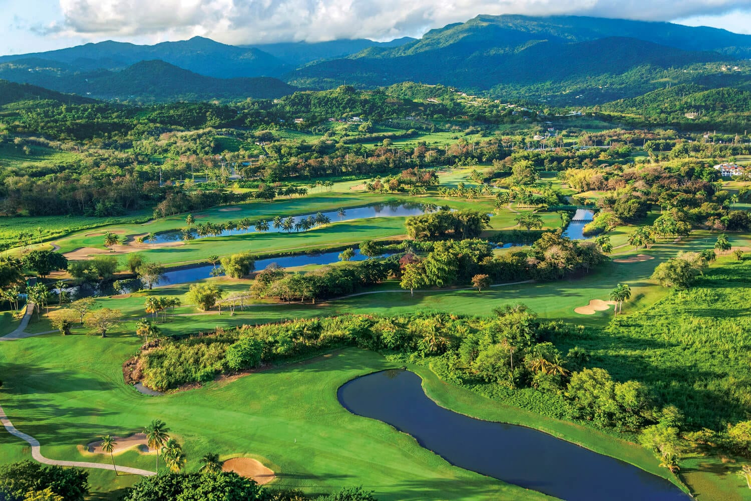 Panoramic view of a pristine golf course with well-manicured fairways, vibrant greenery, and a clear blue sky