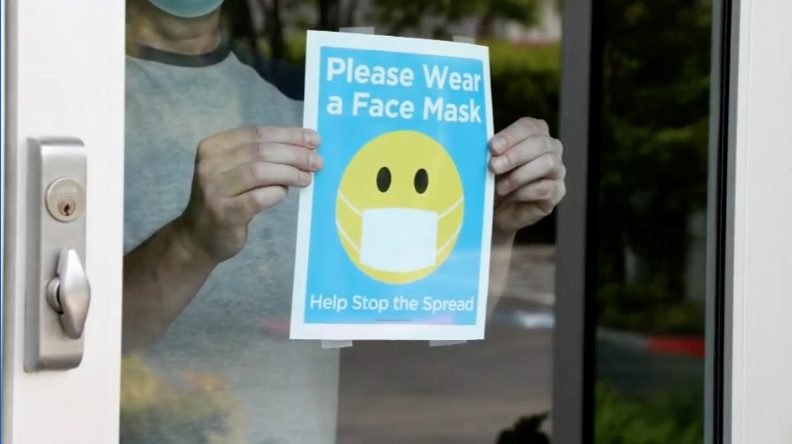 Storeowner putting a Wear a Face Mask sign on window