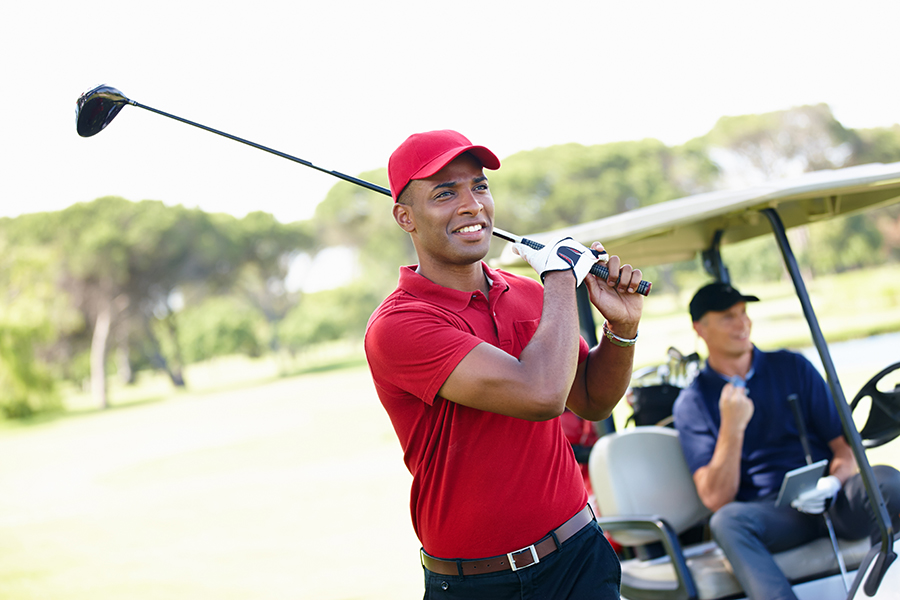 Shot of a young man taking a shot while his friend congratulates him from the golf cart in the background