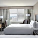 Photo of a New Orleans Marriott guest room showing a window, two beds, desk with chair, arm chair and lamps.
