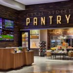 Interior photo of New Orleans Marriott, behind Fahrenheit 55, is the entry to Canal Street Pantry. In the photo are display tables of food, and behind those are refrigerators of beverage options.