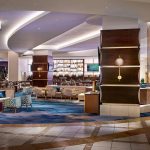 Photo of New Orleans Marriott inside. Next to the check-in desks is the 55 Fahrenheit restaurant and bar. Photo shows mixed seating options, bar, and disply of alcohol behind bar.