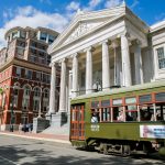 St Charles Streetcar stopped on St Charles Street in front of the Gallier Hall, a Greek Revival architectural style building.