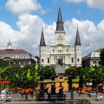 Three horse-drawn carriages are in the foreground parked in front of The Cabildo, the St, Louis Cathedral, and the Presbytere in New Orleans.