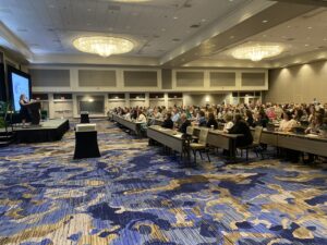 Large ballroom with 500+ attendees listening to speaker onstage