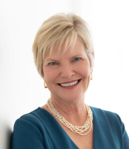 Dr. Kay Kennedy headshot, woman with short, blonde hair, wearing teal blouse and jewelry