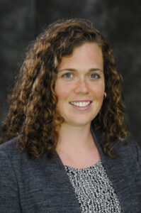 Hannah Siburt headshot, woman with brown curly hair wearing gray jacket and blouse