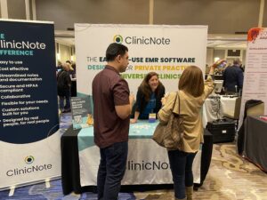 Two attendees talking to the representative at the ClinicNote booth at the 2024 Welcome Reception.