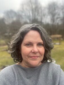 Jennifer Mackey headshot, women with above shoulder length curly gray hair, gray sweater