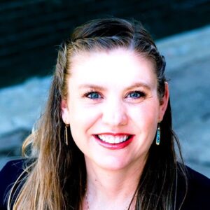 Lindsey Jorgensen headshot, woman long brown hair, teal jewelry, black jacket