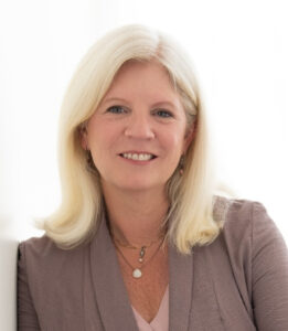 Susan Campis headshot, woman with shoulder-length blonde hair, taupe blouse and jewelry