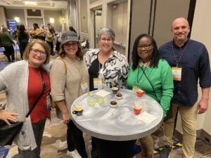 Five attendees gathered around a hightop table with desserts and beverages at the 2024 Welcome Reception.