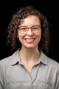 Laura Chapman headshot, white female, shoulder-length, brown curly hair, glasses, gray collared blouse