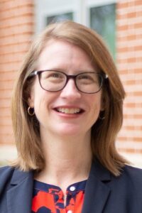 Susan Gordon Hickey headshot, whit4e female, strawberry blonde shoulder length hair, navy suit jacket, floral blouse