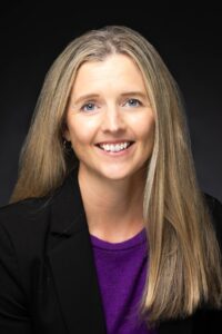 Sandra Kemper headshot. White female long blonde hair, black suit jacket, purple blouse