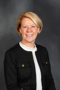 Tena McNamara headshot. female with short blonde hair, black jacket, white blouse