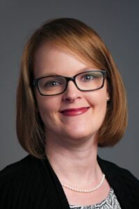 Tara Davis headshot, white female, short red hair, black cardigan, blouse