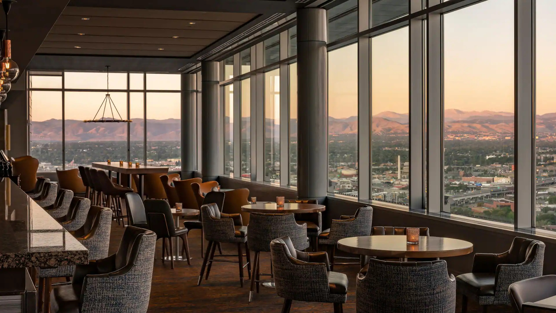 wall-to-wall windows overlooking Denver and mountains, inside is bar with chairs, and tables
