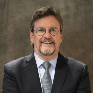 Man with brown hair, wearing glasses, and a suit, dress shirt and tie