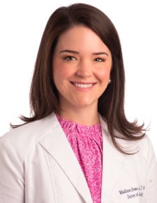 Woman with below the shoulder, straight brown hair, smiling, wearing pink blouse and white lab coat
