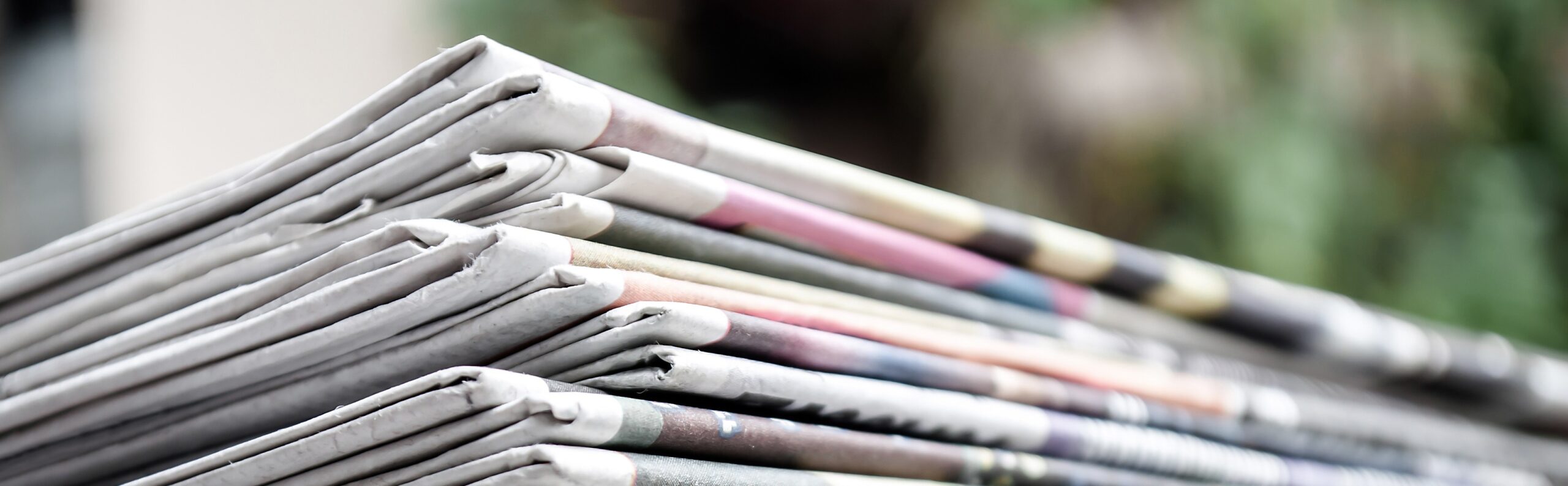 Newspapers folded and stacked on the table with gardenor green background. Closeup newspaper and selective focus image. Time to read concept..