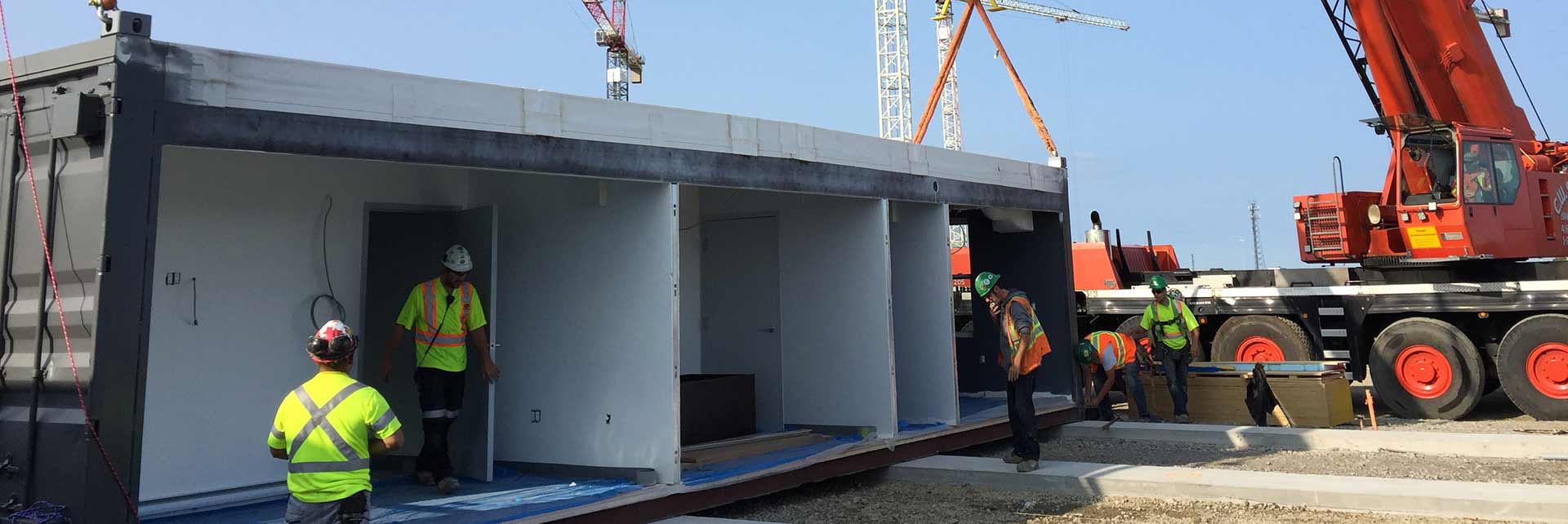 Modular construction workers putting the finishing touches on a building module with a crane in the background ready to pick up the finished product