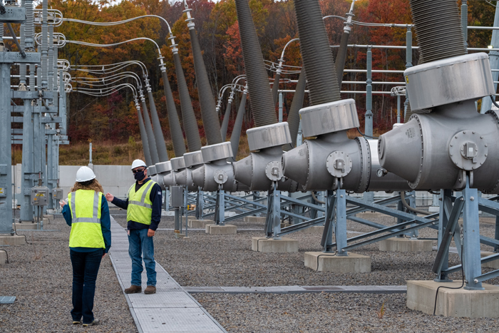 Two PPL workers standing next to power grid